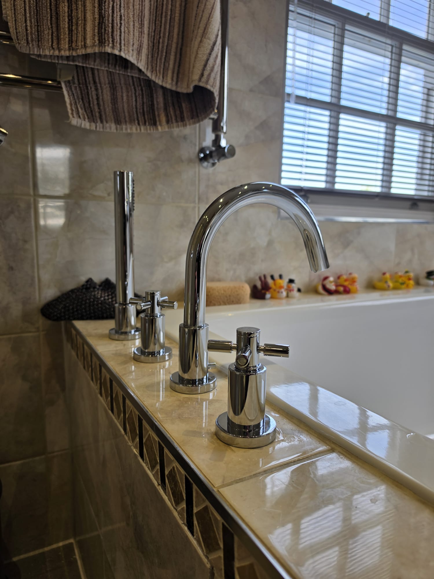 New chrome deck-mounted bath taps with hand shower running, fitted on a tiled bath surround, Surrey
