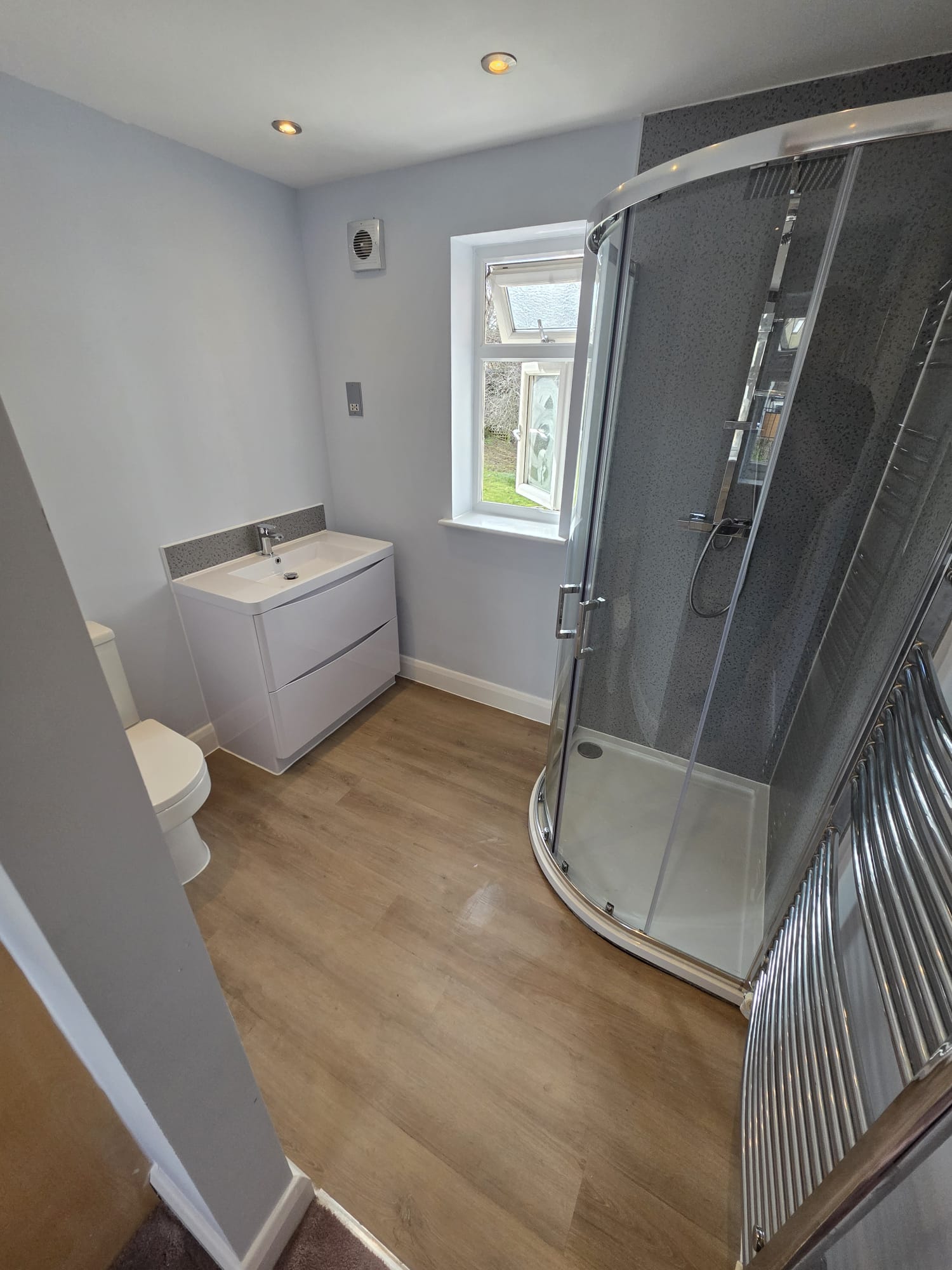 Modern bathroom installation with quadrant shower enclosure, vanity unit and wood-effect flooring, Surrey